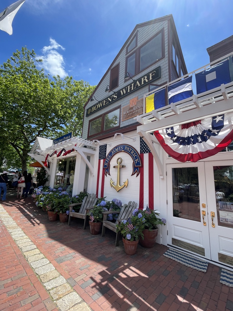 A shingled building on Bowen's Wharf in Newport, dressed in red, white and blue bunting with hydrangeas along the brick walk.