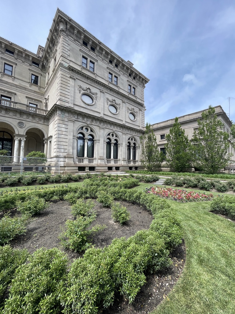 The Breakers mansion in Newport, its limestone façade rising behind curved garden beds and a green lawn.