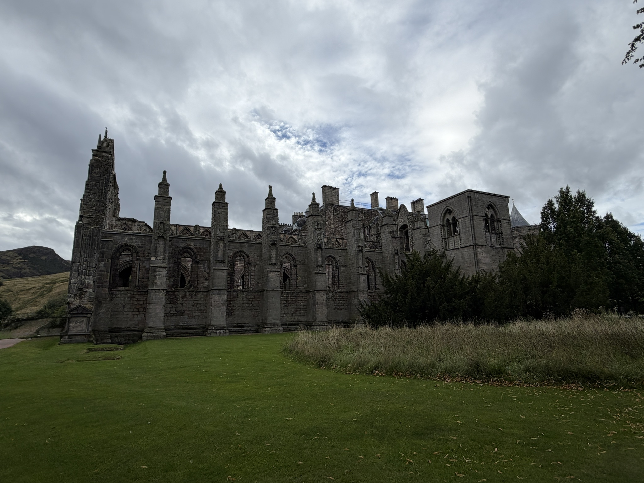 The ruins of Holyrood Abbey in Edinburgh beneath a wide, cloudy sky.