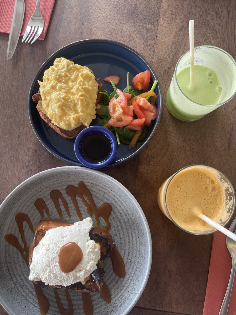 Breakfast at Lulu's Corner from above: scrambled eggs on toast with a tomato and spinach salad, caramel-drizzled French toast topped with cream, and two fresh smoothies.