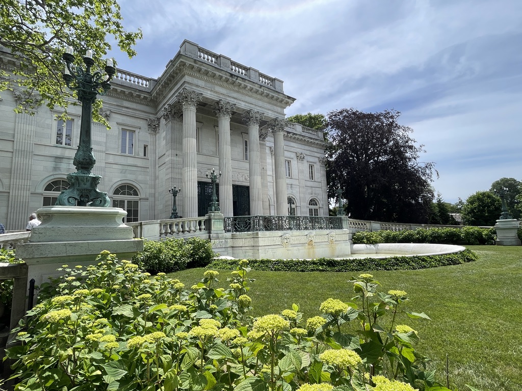 Marble House in Newport, framed by hydrangeas and a manicured lawn under a summer sky.