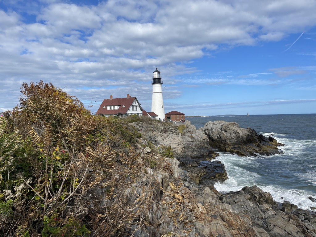 A white lighthouse on a rocky headland above the sea in Portland, Maine.