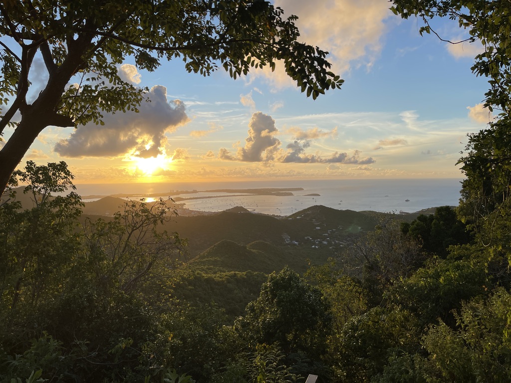 The sun setting over the sea beyond green hills in St. Martin.